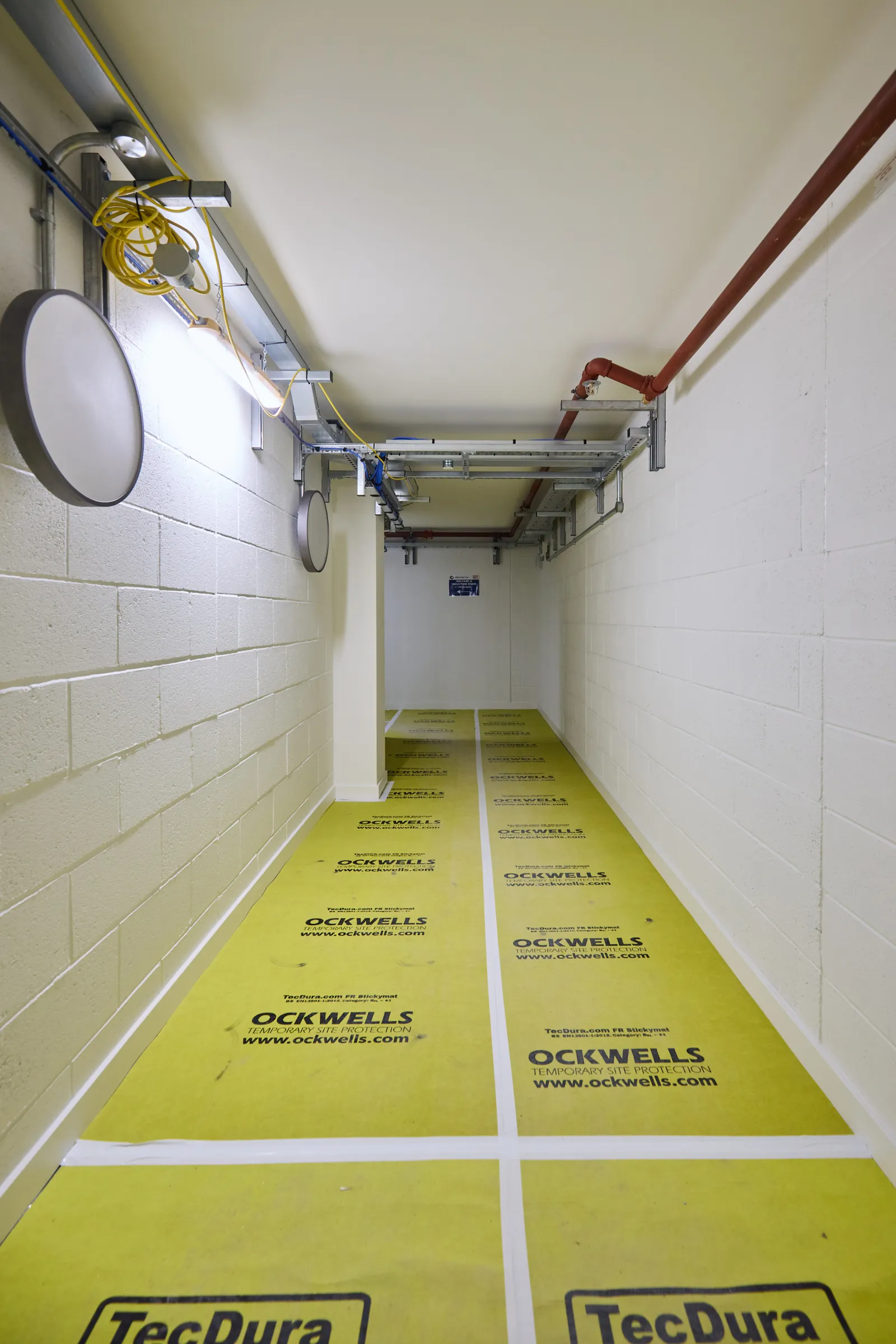 Narrow corridor under refurbishment with yellow protective floor covering.
