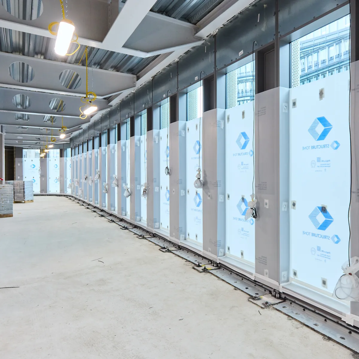 Bright corridor with glazed partitions and exposed ceiling services during construction.