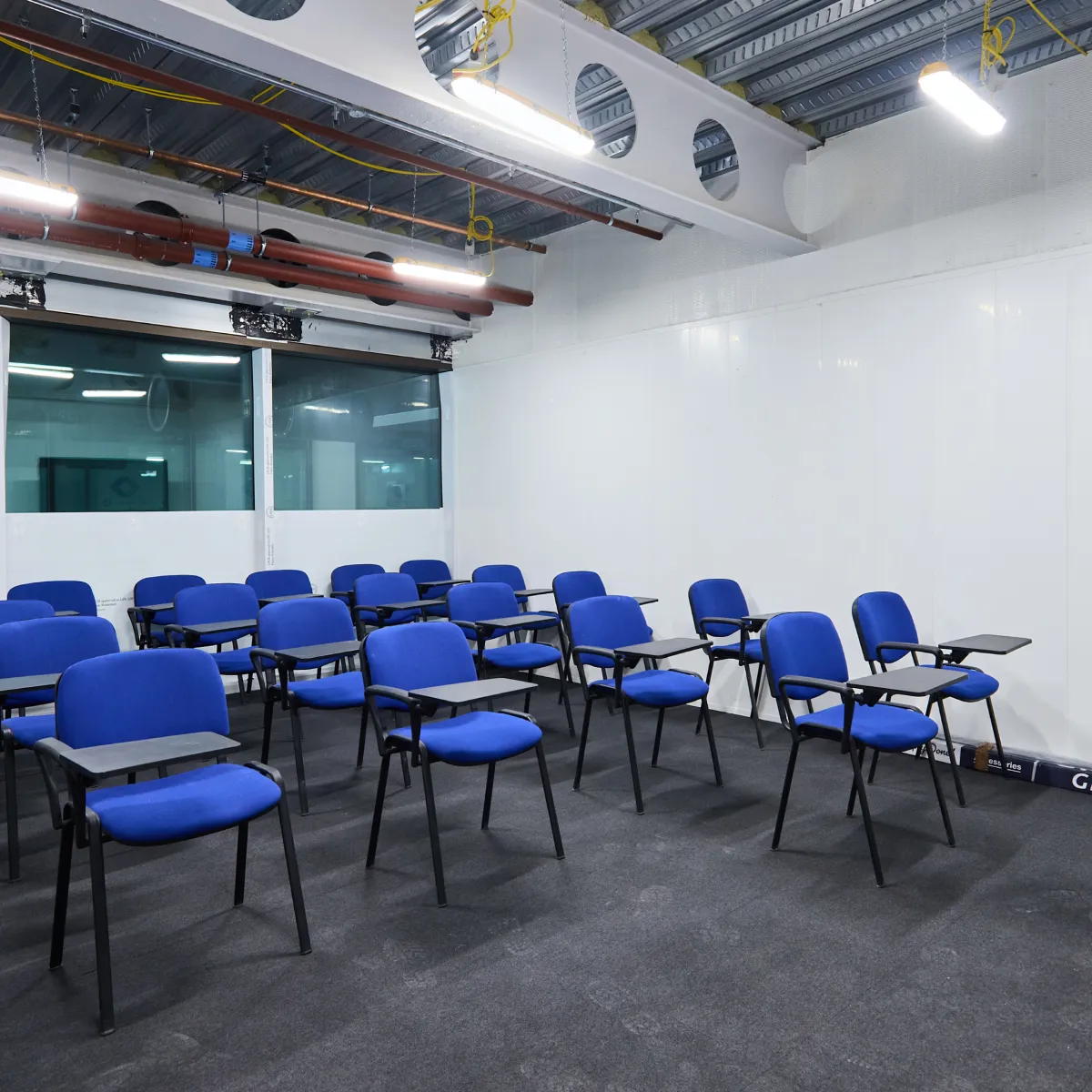 Meeting room with blue chairs and exposed ceiling services.