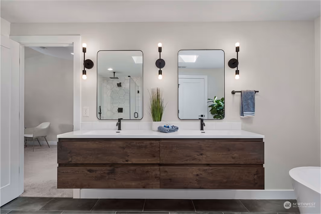Sleek double-sink vanity with rich wood cabinetry, white countertops, matte black faucets, and twin mirrors, each flanked by modern vertical light fixtures.
