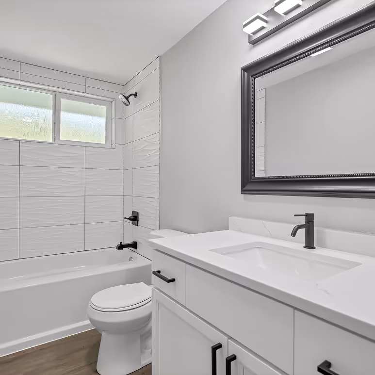 Updated bathroom with textured tile tub surround, white vanity with black hardware, and modern lighting.