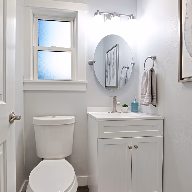 Small, modern bathroom featuring a white vanity, round mirror, and brushed nickel fixtures.