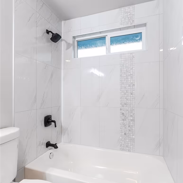 White bathtub and shower with large marble-look tiles and a vertical mosaic accent strip.