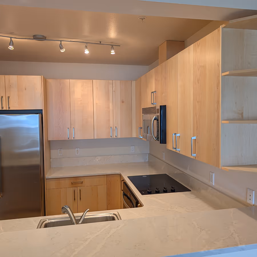Compact kitchen featuring light blonde wood flat-panel cabinets, white quartz countertops, and stainless steel appliances.