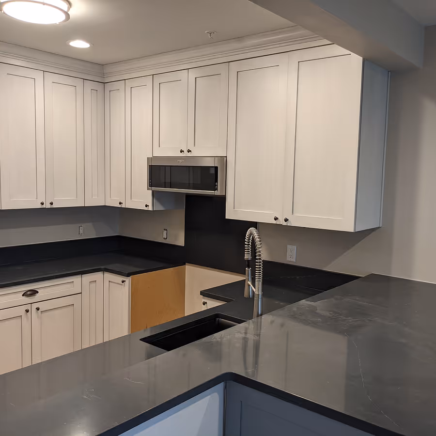 Modern kitchen with white shaker cabinets, dark charcoal countertops, a black undermount sink, and a built-in microwave.