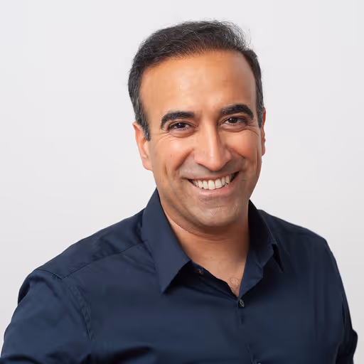 Smiling middle-aged man with short dark hair, wearing a dark blue button-up shirt, against a plain light background.