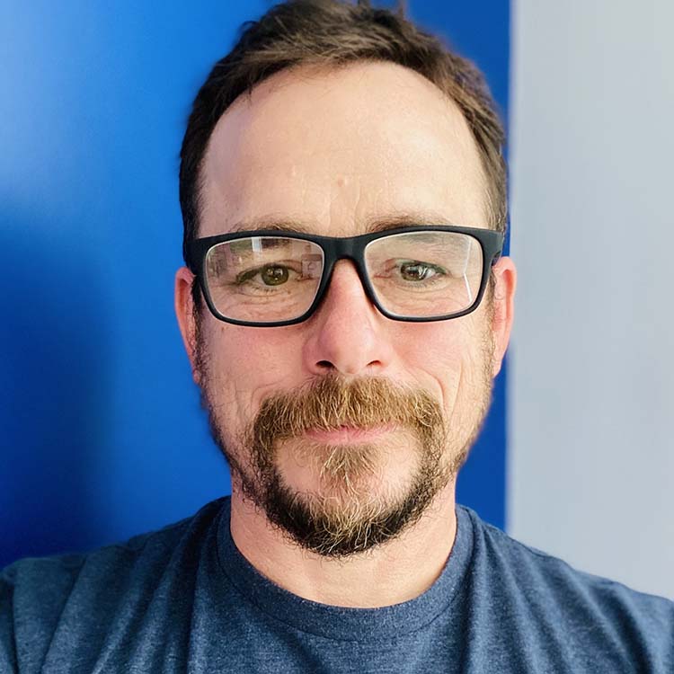 Dave Guthier headshot, in a blue shirt and glasses with blue background
