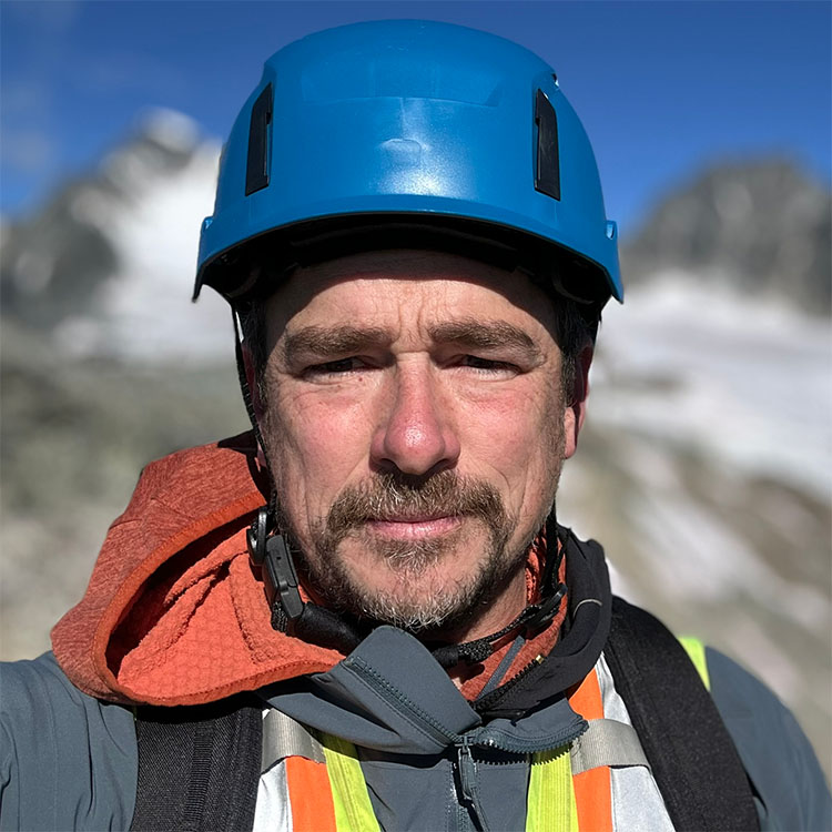 Dave Guthier headshot, wearing a blue hardhat, with mountain background