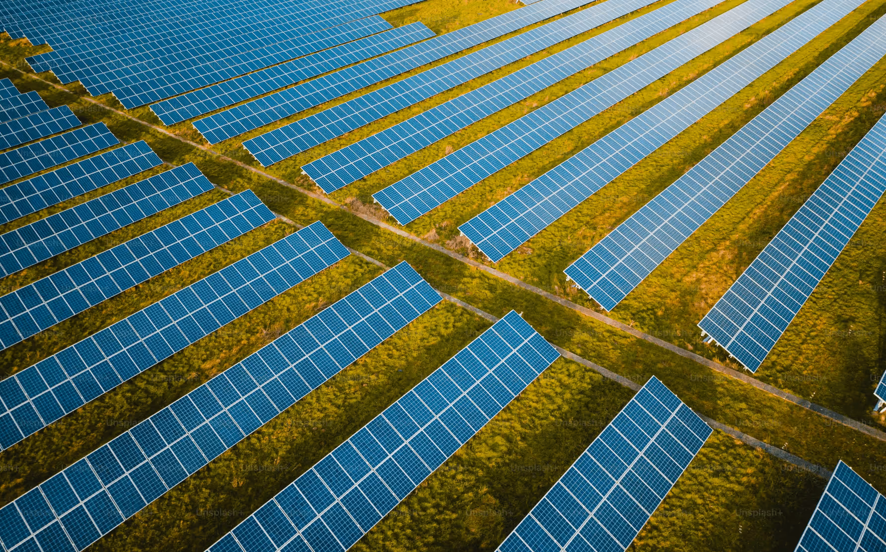 Aerial view of large solar panel arrays installed in rows on green grassy fields.