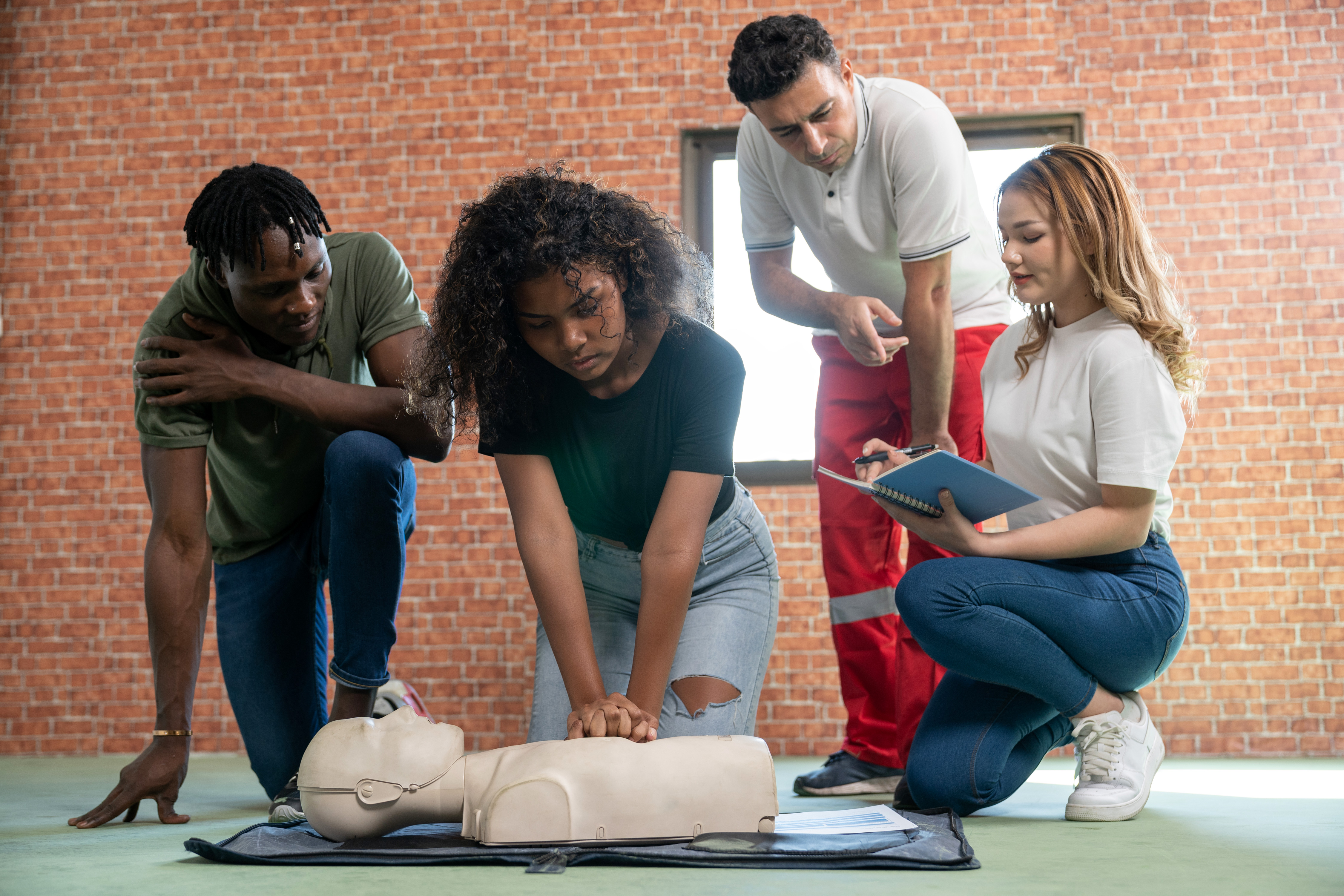 A participant practices CPR on a training manikin while others observe and provide guidance.