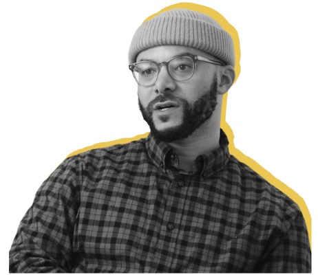 Man with beard and glasses wearing a beanie and checkered shirt, with a yellow outline behind him.