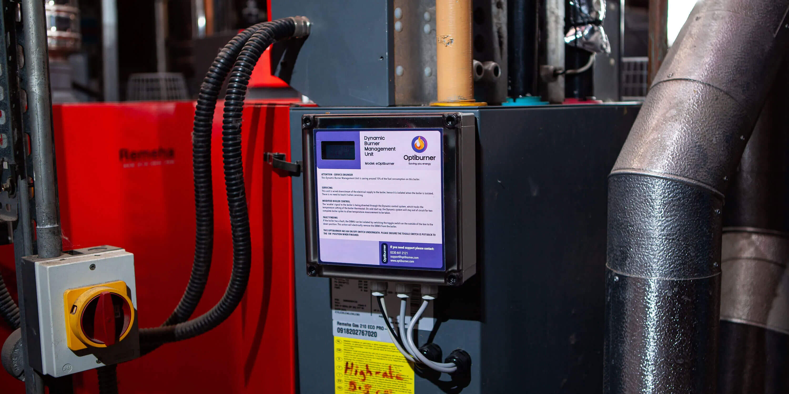 Close-up of an industrial Optiburner dynamic burner management unit mounted on machinery with connected cables and pipes.