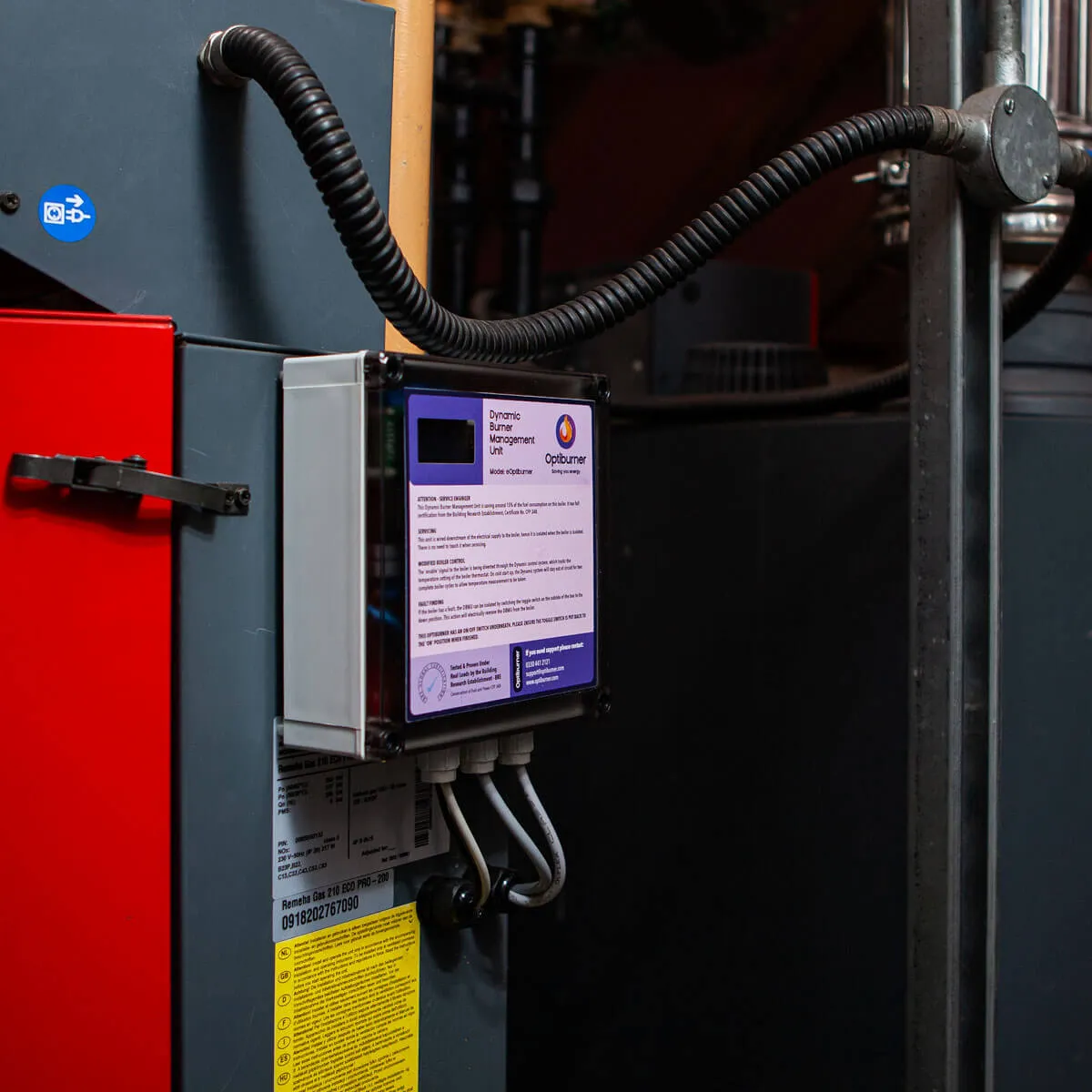 Dynamic Burner Management Unit labeled 'Optiburner' mounted on a gray industrial machine with connected cables and warning labels.