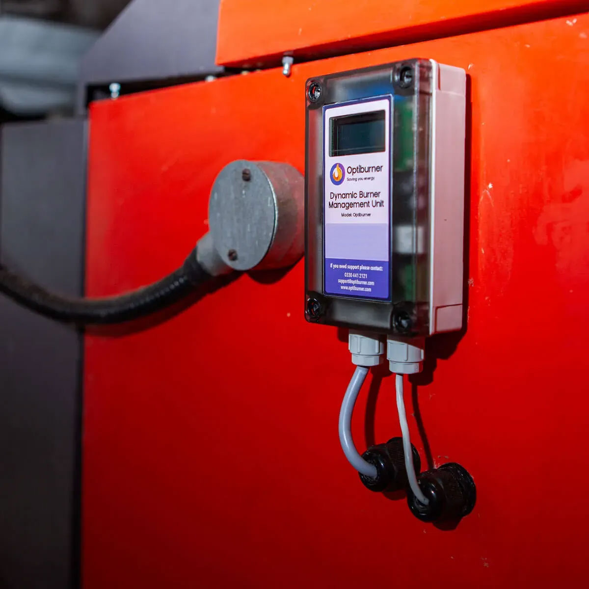 Optiburner Dynamic Burner Management Unit mounted on a red industrial machine with connected cables.
