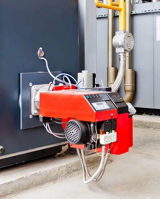Industrial red burner unit attached to a boiler system with connected metal pipes and electrical wiring.