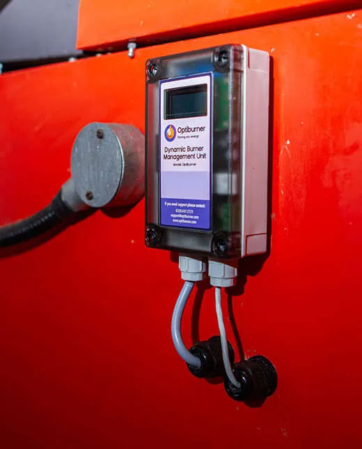 Optiburner Dynamic Burner Management Unit mounted on a red surface with two cables connected at the bottom.