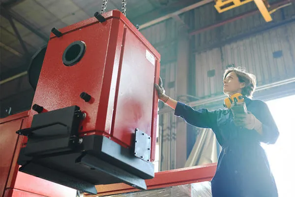 Woman wearing safety gear inspecting large red industrial equipment in a warehouse.