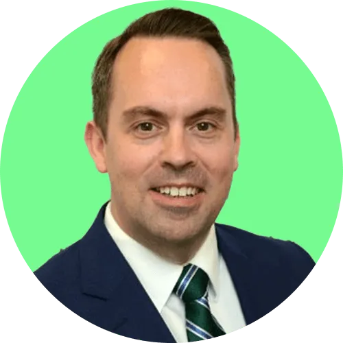 Portrait of a smiling man in a navy suit, white shirt, and green striped tie with a light green background.