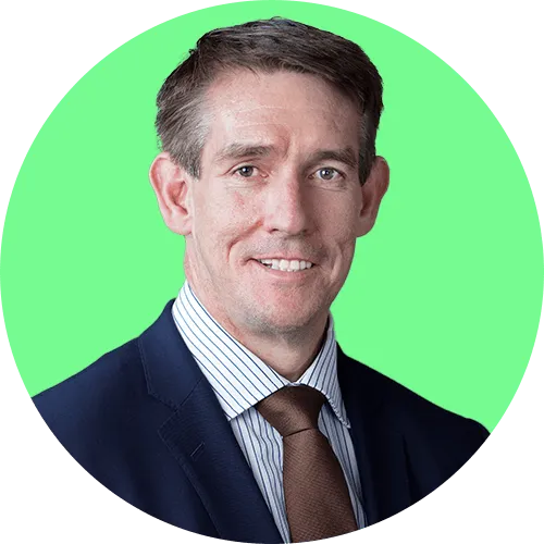 Smiling man wearing a navy suit, striped shirt, and brown tie against a bright green circular background.