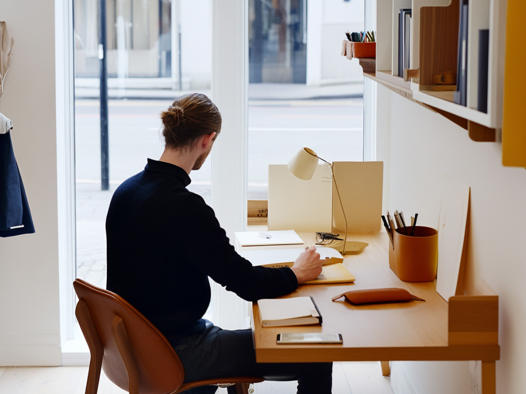 Person writing at a wooden desk in a bright studio, planning a brand strategy