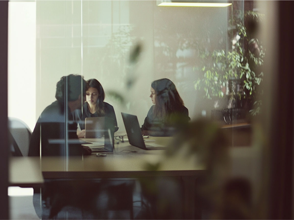 Team meeting at a conference table with laptops, seen through glass