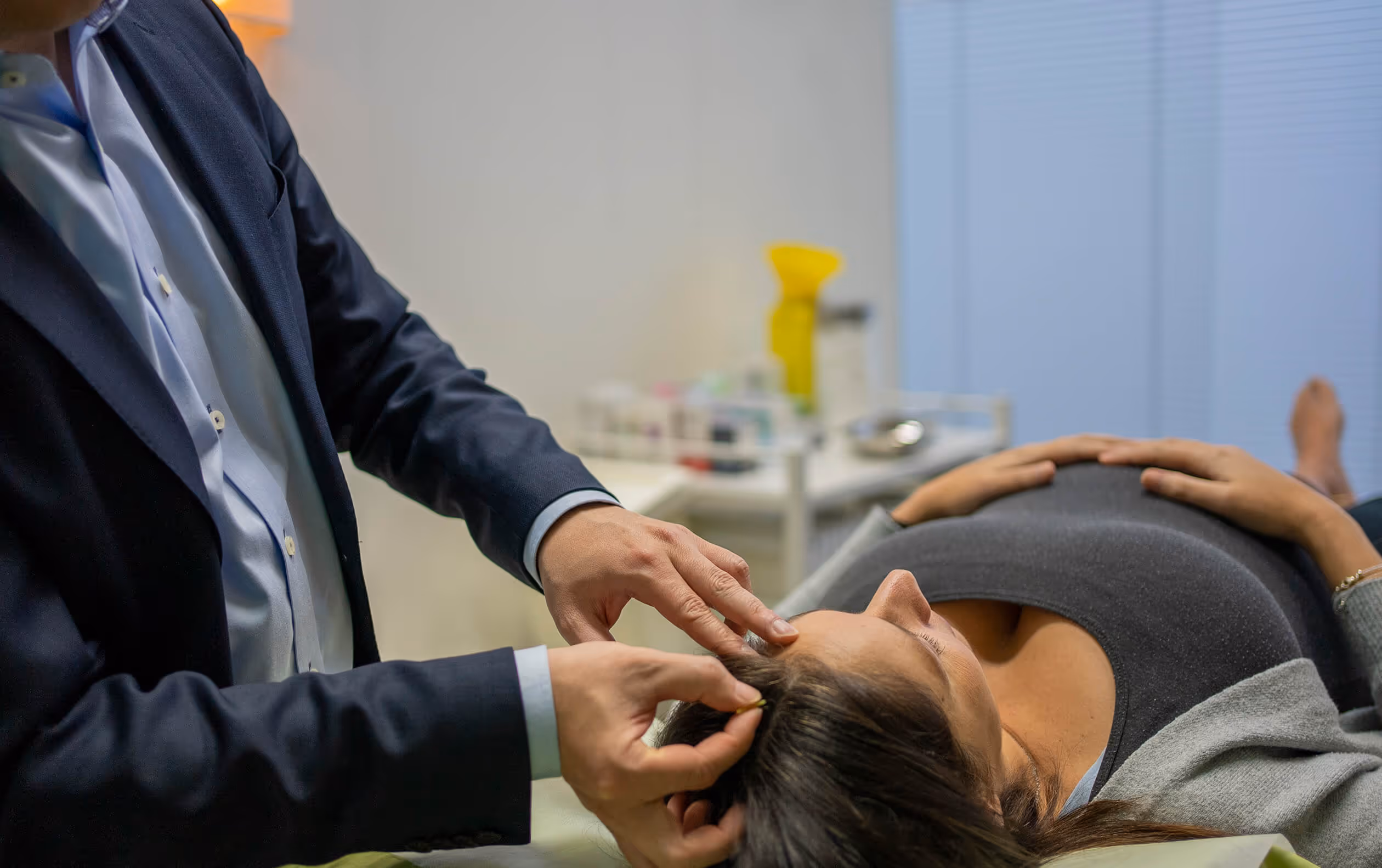 Woman lying on a medical bed receiving acupuncture treatment on her head from a practitioner.