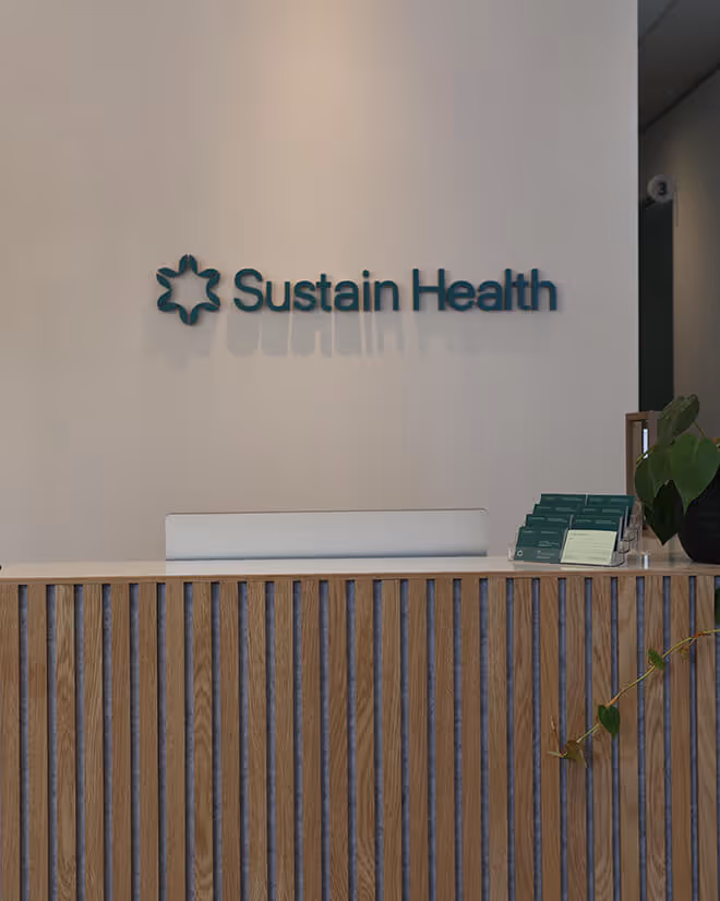 Reception area with a wood-paneled desk and the Sustain Health logo on the wall behind it.