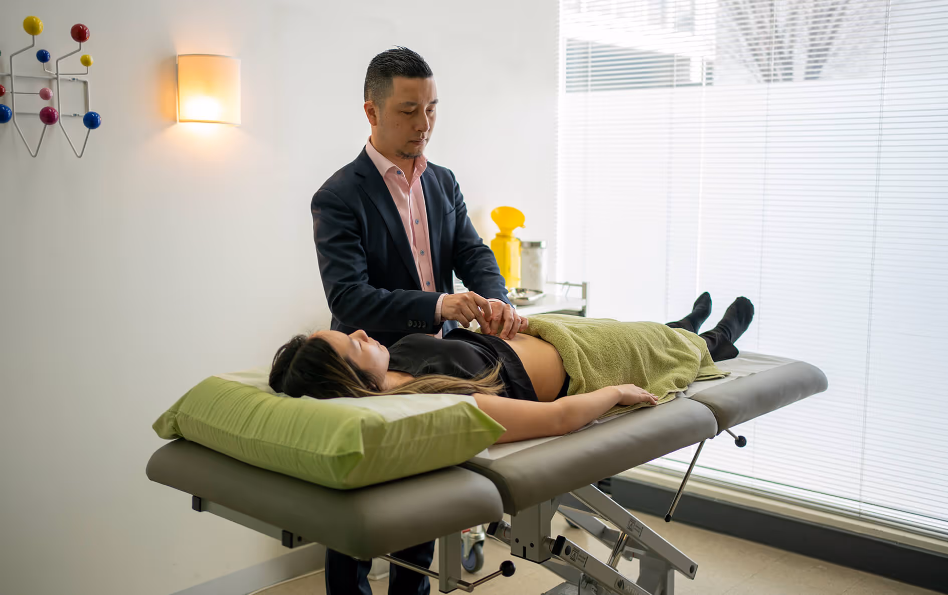 Male doctor examining a woman's abdomen as she lies on a medical examination table in a clinic.