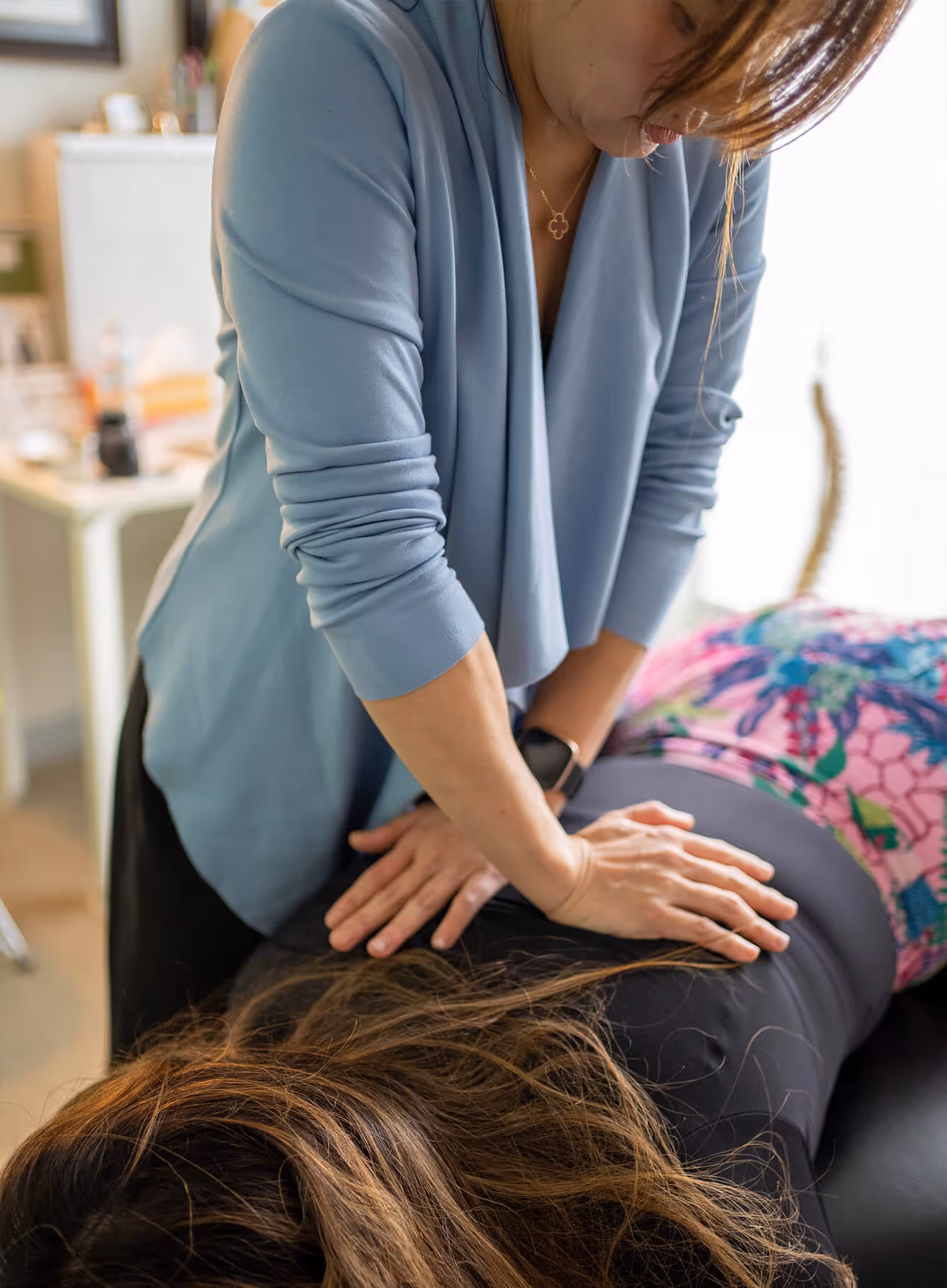 Chiropractor in blue jacket performing a back adjustment on a patient lying face down.