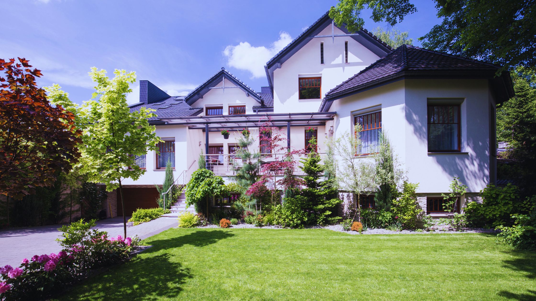 "A modern suburban home with a spacious driveway and double garage, set against a vibrant sunset sky, featuring well-maintained landscaping and a cozy porch light illuminating the entryway.