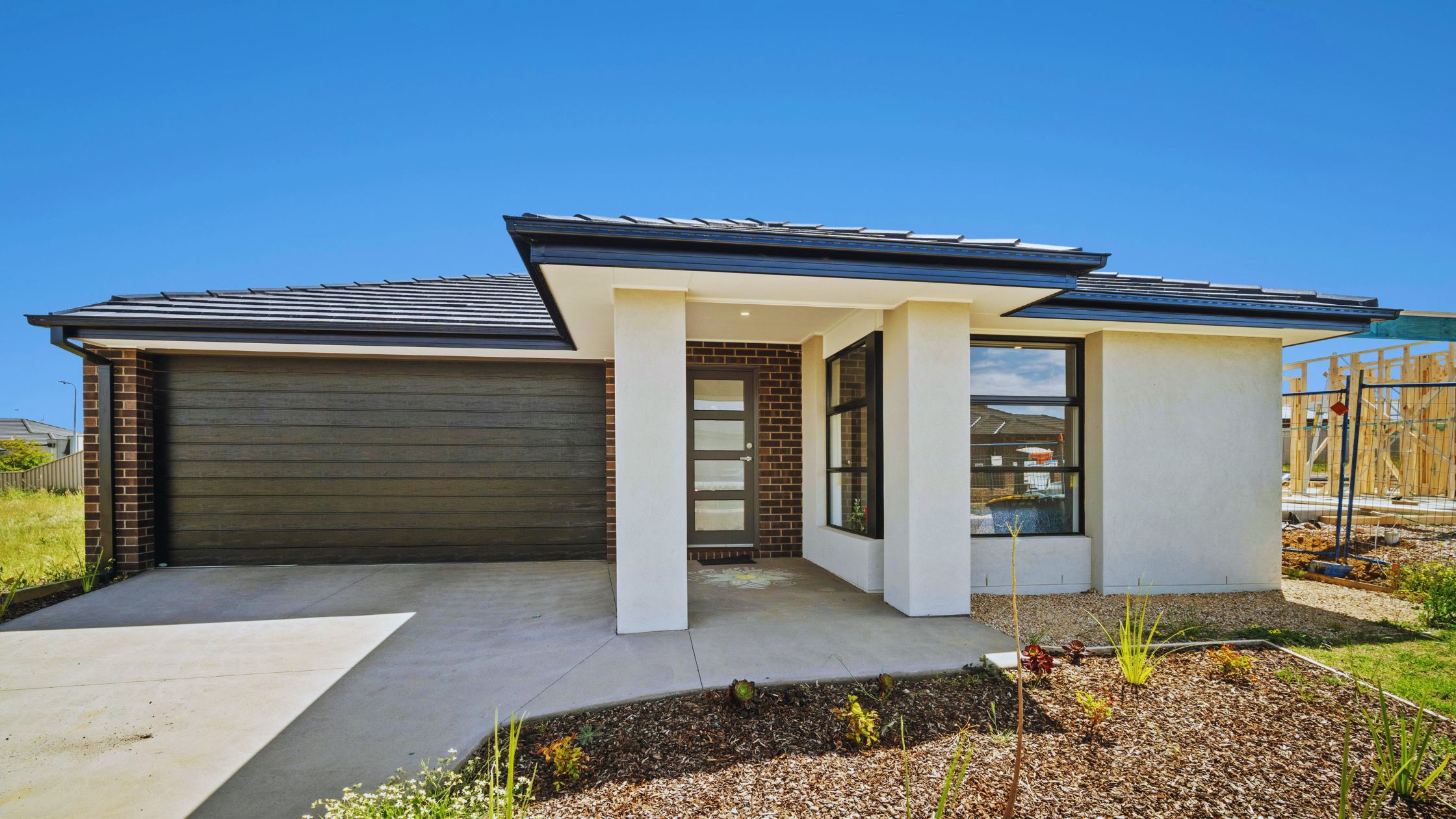 "A modern suburban home with a spacious driveway and double garage, set against a vibrant sunset sky, featuring well-maintained landscaping and a cozy porch light illuminating the entryway.