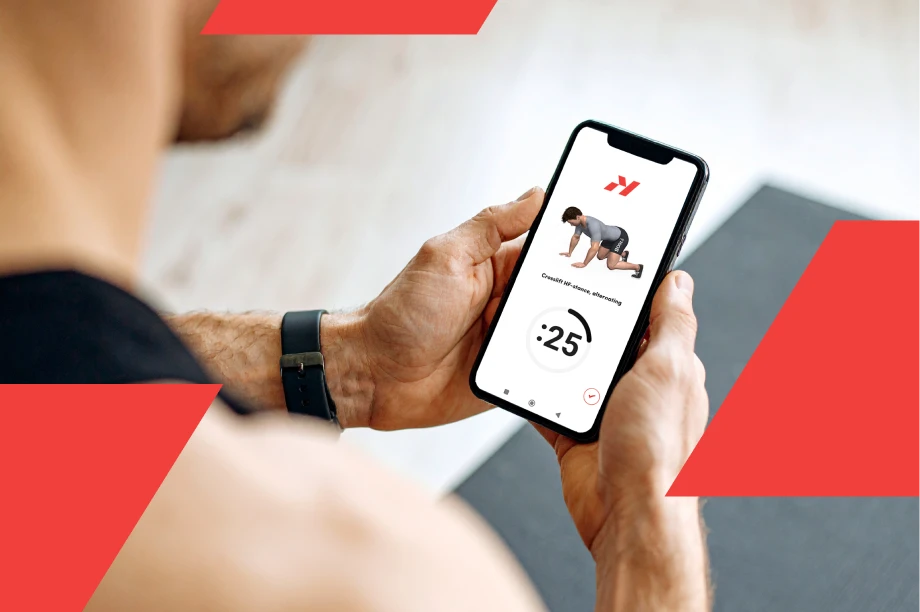 Man holding a smartphone displaying a fitness app with a workout timer and exercise demonstration on the screen.