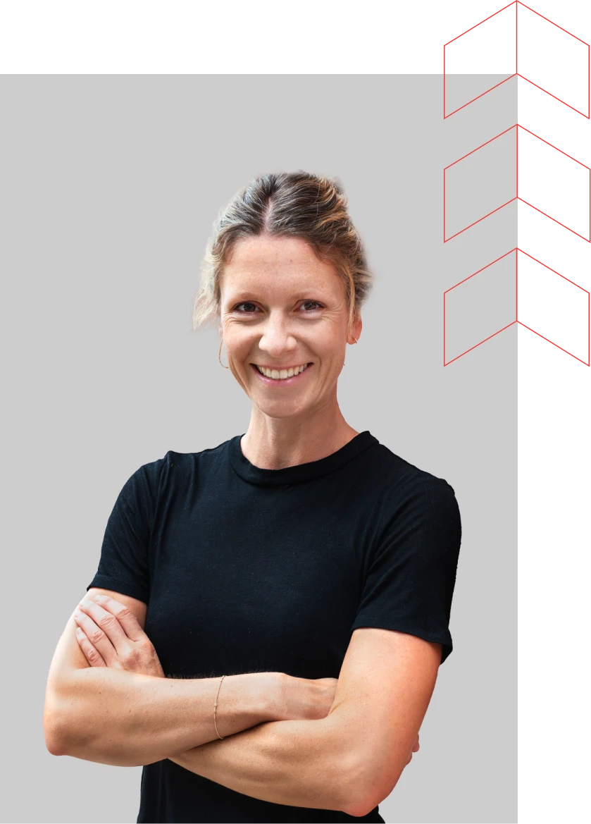 Maria Kilian, a smiling woman with blonde hair tied back, wearing a black short-sleeved top, standing with arms crossed against a plain grey background.