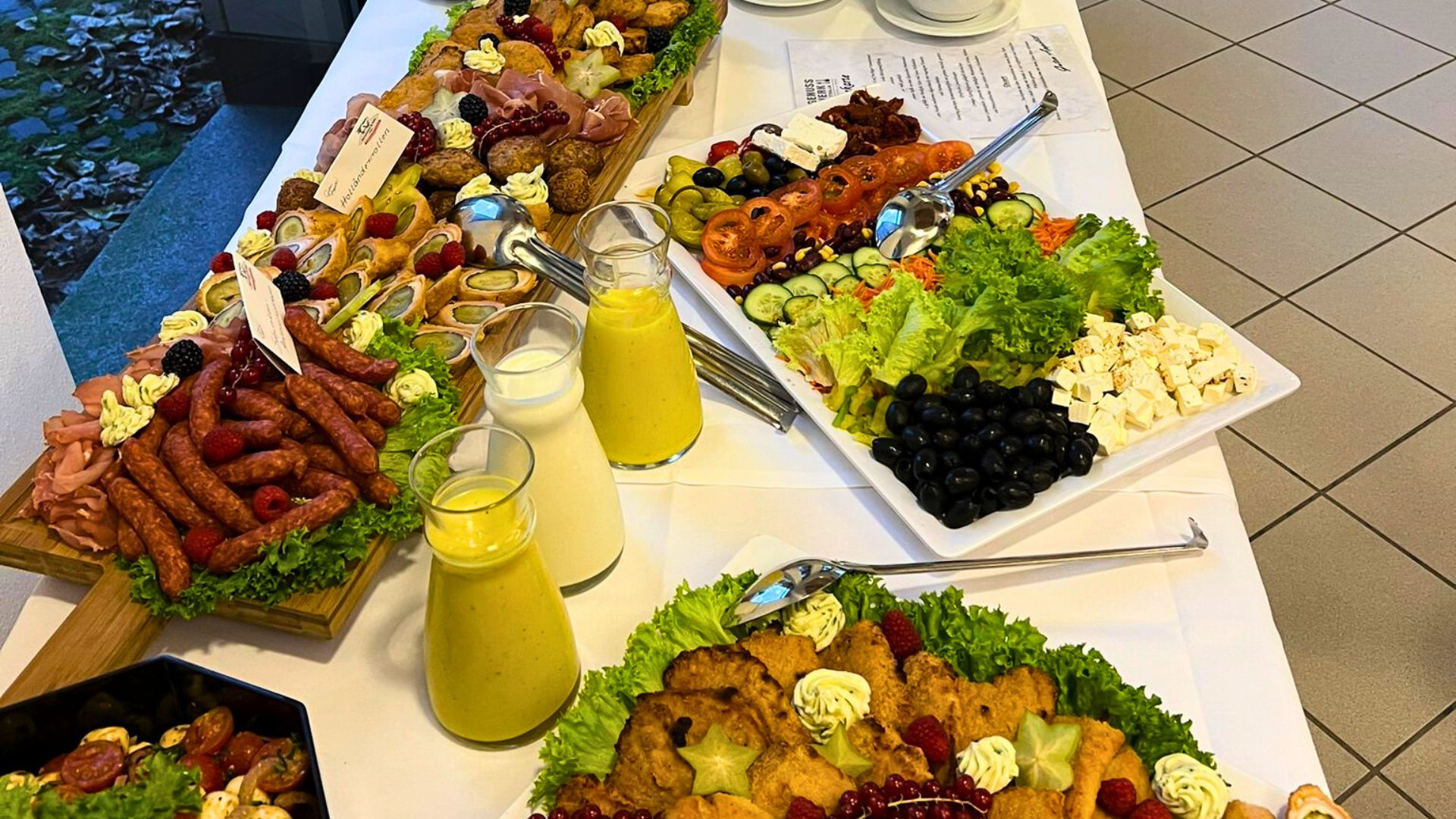 Buffettisch mit vielfältigen Speisen, frischen Salaten, Aufschnitt, Käse und Soßen, appetitlich angerichtet für eine Firmenfeier.