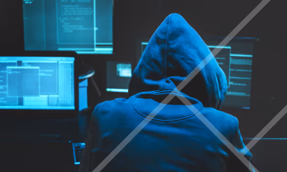 Image of hooded figure infront of multiple computer screens - First Technology Cyber Security Solutions