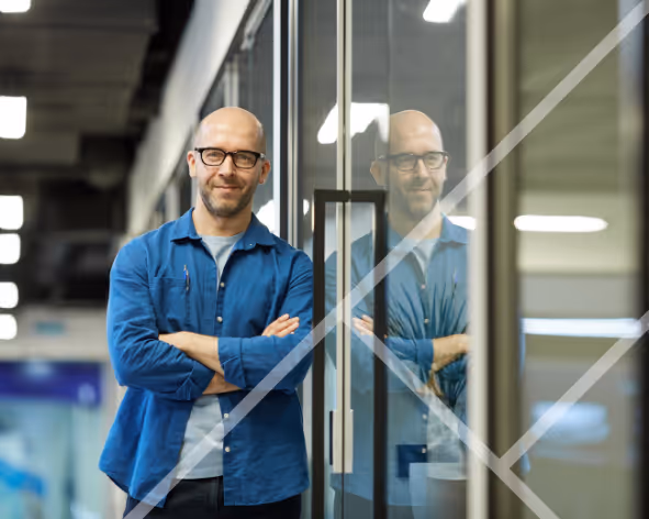 A professional man leaning against a glass partition with arms crossed