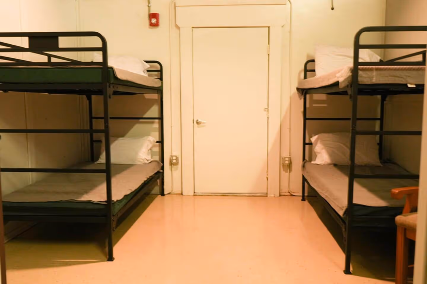 Barn bunkhouse room showing two black metal bunk beds opposite each other, each with pillows and gray bedding, and a door at the back.