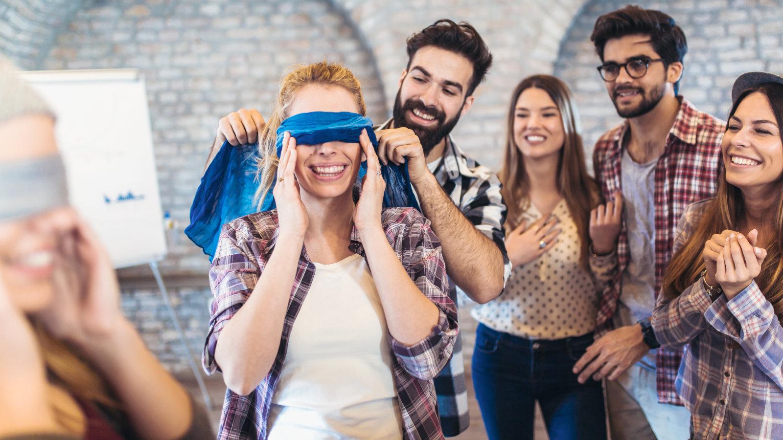 A group of colleagues engaging in a team-building exercise with one team member being blindfolded, showcasing interactive dynamics at The MacArthur.