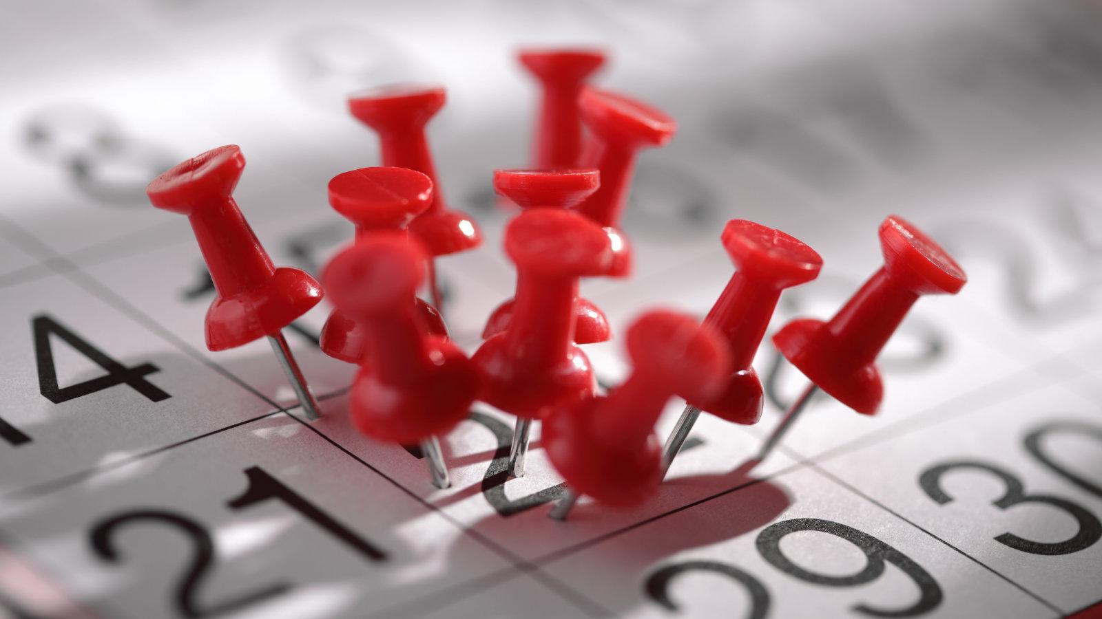 Red push pins marking crucial dates on a grayscale calendar, highlighting detailed event planning.