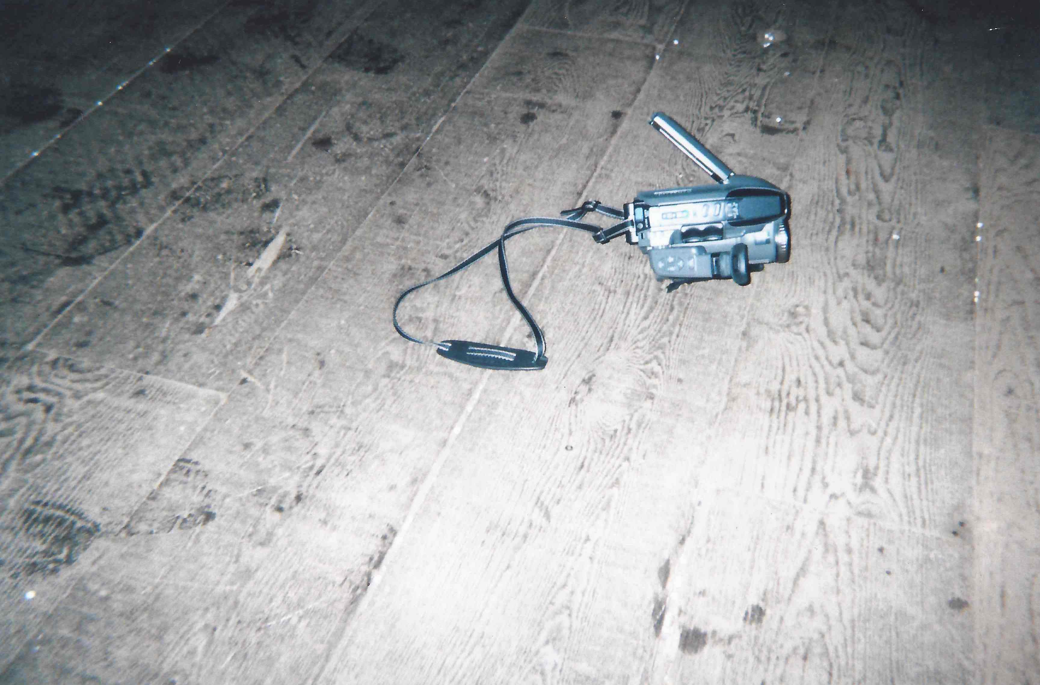 A vintage handheld video camera lying on a wooden floor.