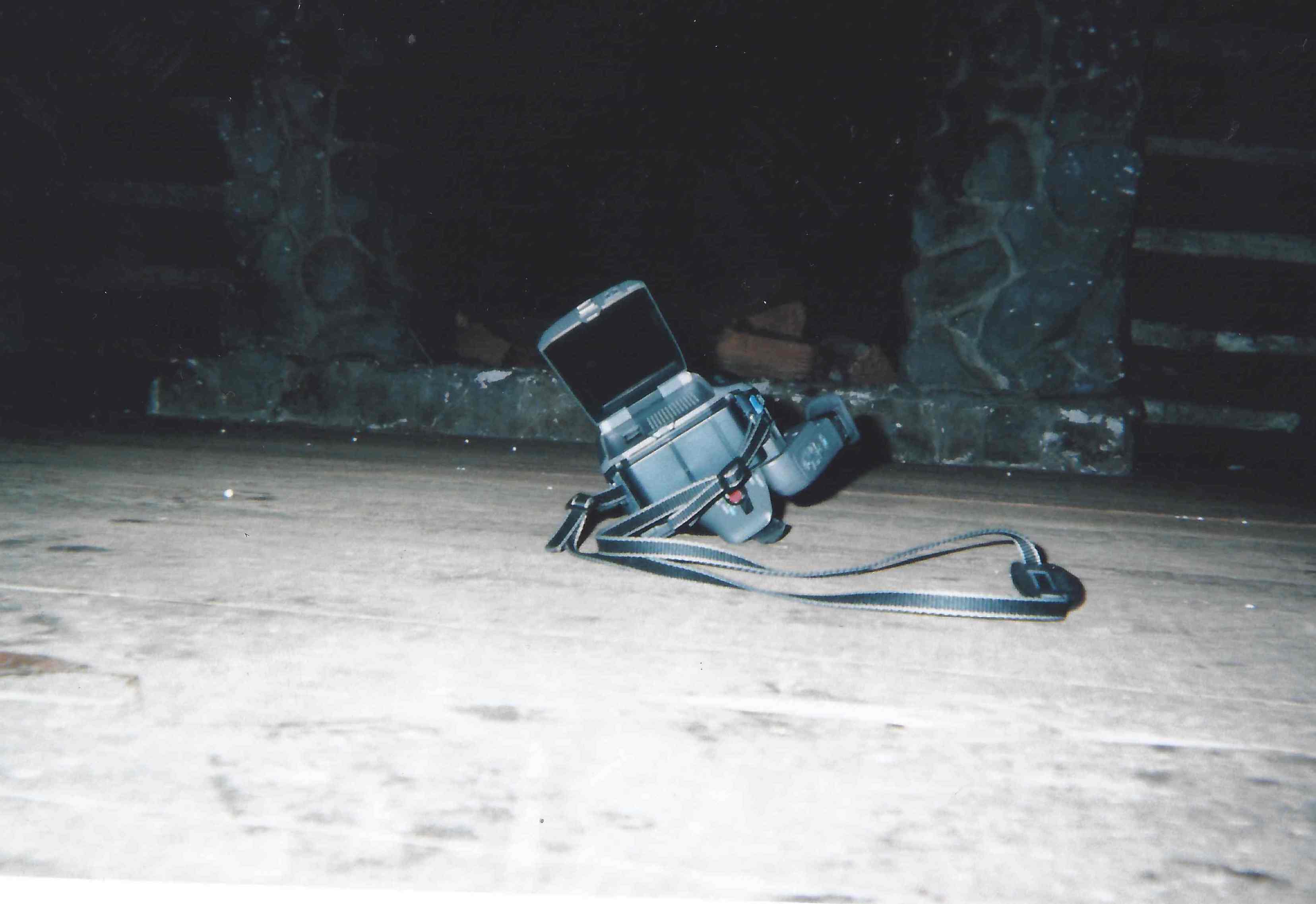 Old handheld video game console with an open screen and wrist strap placed on a wooden surface indoors.