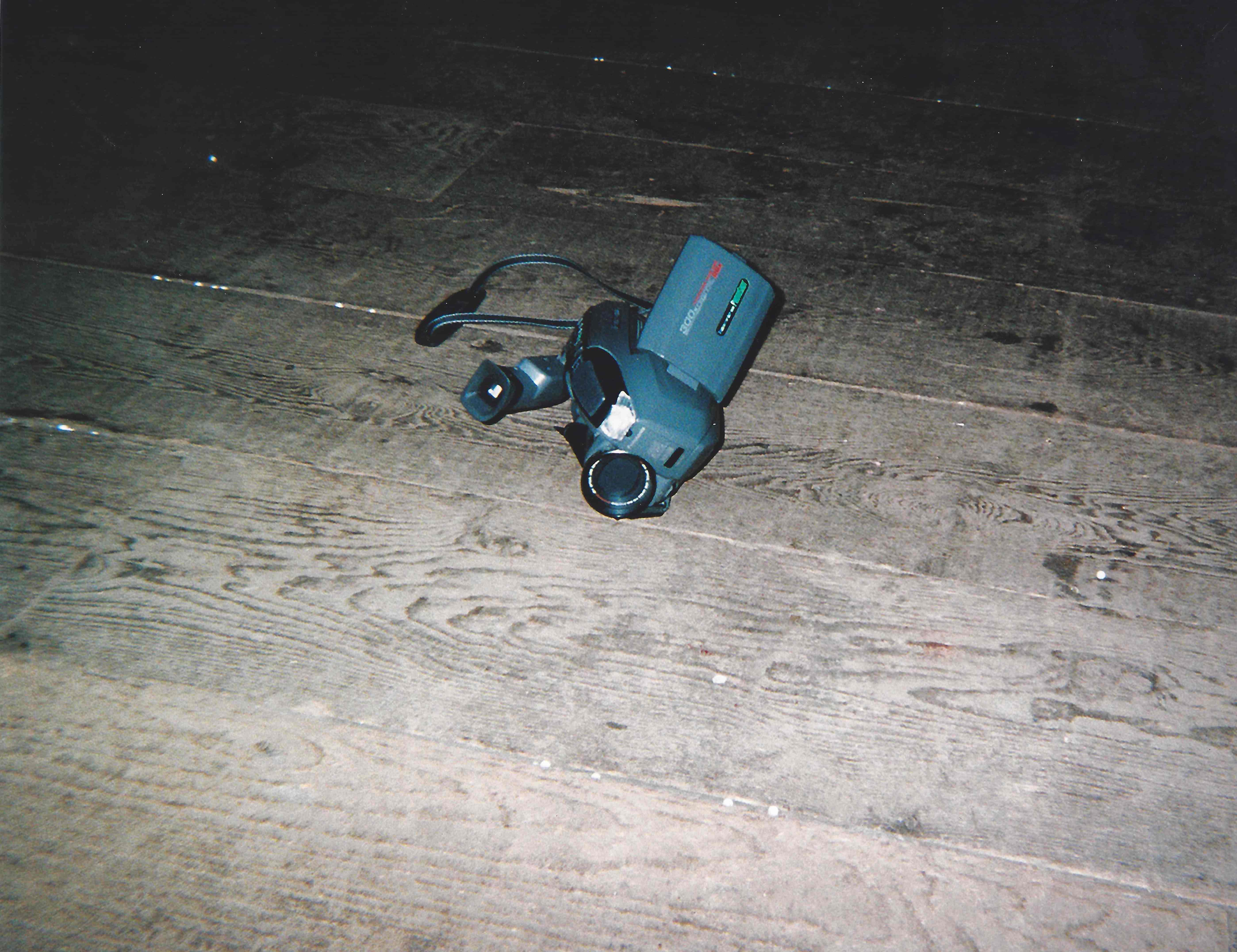 A small handheld camcorder with flip-out screen lying on a wooden floor.