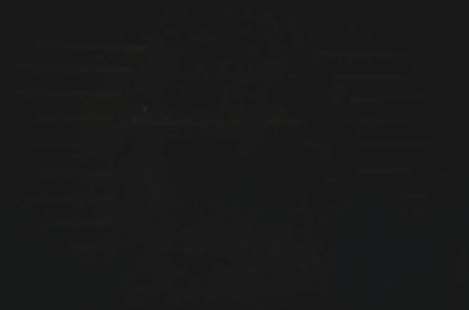 Black cat sitting on a wooden bench in dim lighting.