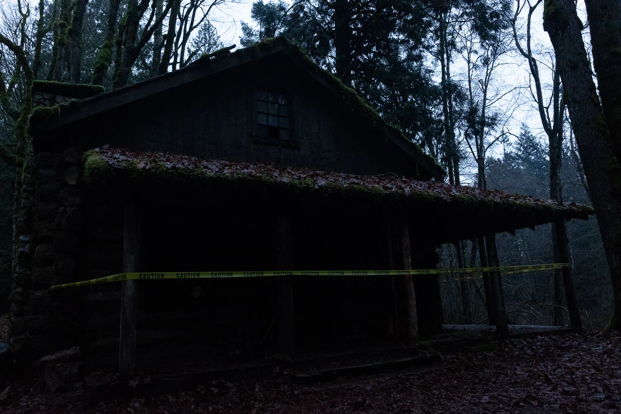 Dark wooden cabin in forested area with caution tape across the front porch.