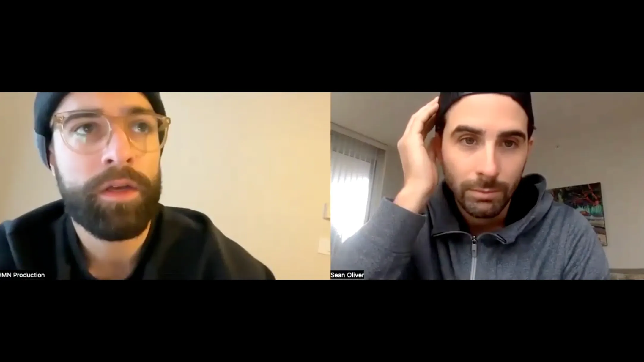 Split-screen video call showing two men with dark hair and beards; the man on the left wears glasses and a beanie, the man on the right wears a cap backwards and adjusts it with his hand.