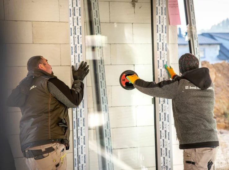 Dva řemeslníci instalují do novostavby nové okno