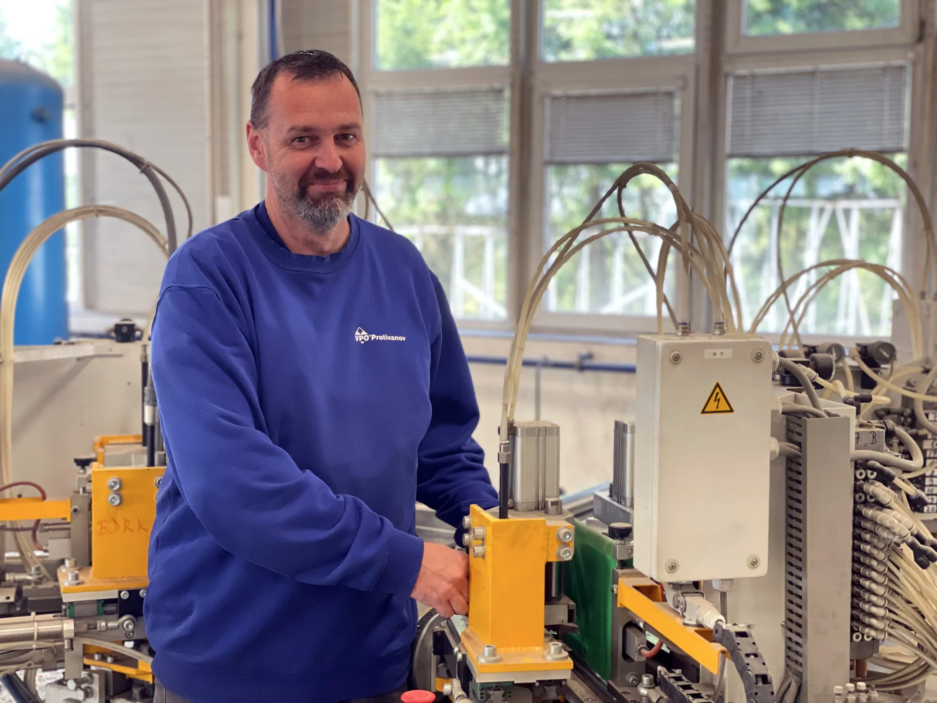 Technik údržby obsluhuje výrobní stroj ve výrobně oken a dveří