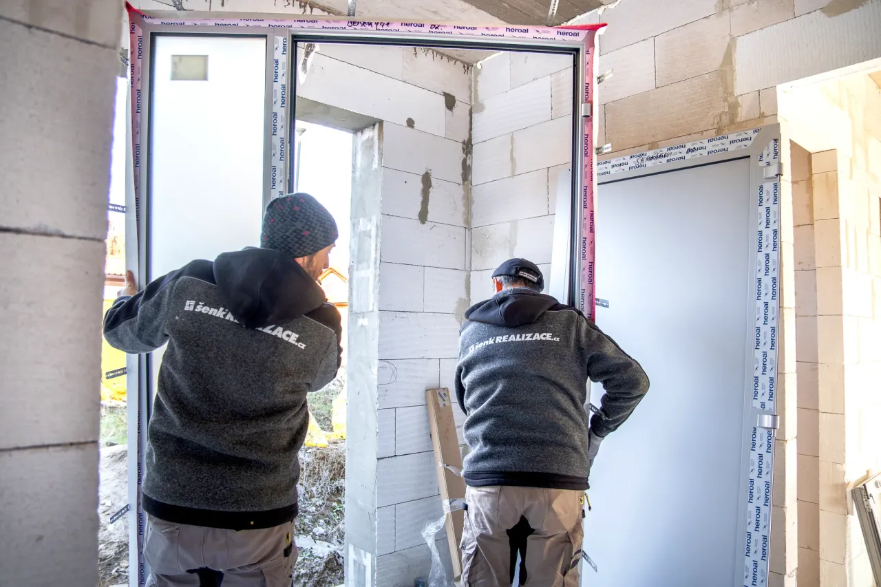 Dva muži montují vstupní dveře v novostavbě