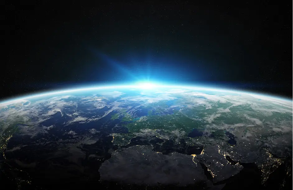 View of Earth from space showing Europe, North Africa, and the Middle East with city lights and sunrise on the horizon.