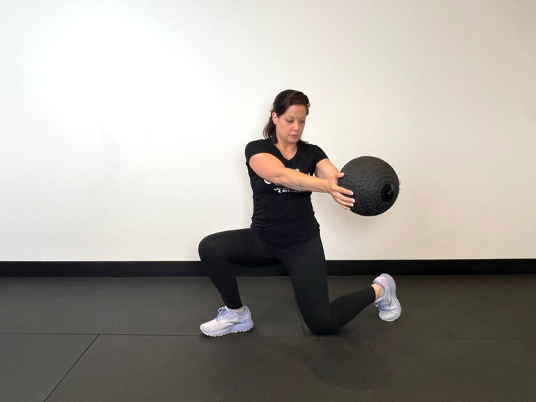 Coach in lunge position, twisting to the left with arms straight out holding medicine ball.